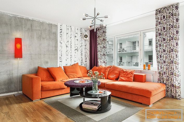 Stilul scandinav este inerent în utilizarea culorilor calde în designul interior. Sofa moale din portocaliu arată organic pe fundalul zidurilor unei nuante gri-gri.