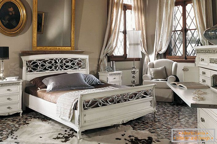 Cerința de bază a stilului baroc este observată. Într-un dormitor spațios, cu tavane înalte, mobilierul din lemn alb contrastează cu ramele întunecate ale ferestrelor.