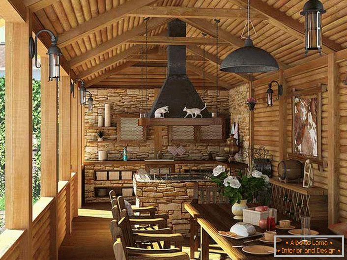 O bucătărie mică cu grătar pe veranda unei case de țară. Stilul de țară este evidențiat, în primul rând, prin decorarea pereților și a tavanului cu un cadru din lemn.