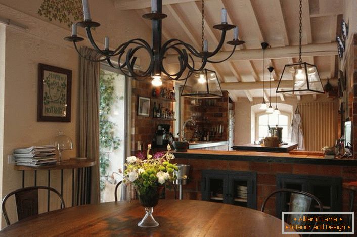 Zona de luat masa și bucătărie este decorată în stil rustic. Ceea ce merită menționat este un candelabru deasupra mesei, care luminează spațiul cu ajutorul lumanarilor obișnuite. Idee subțire de design, deoarece în cameră există, de asemenea, o iluminare tradițională, care lucrează din rețeaua electrică.