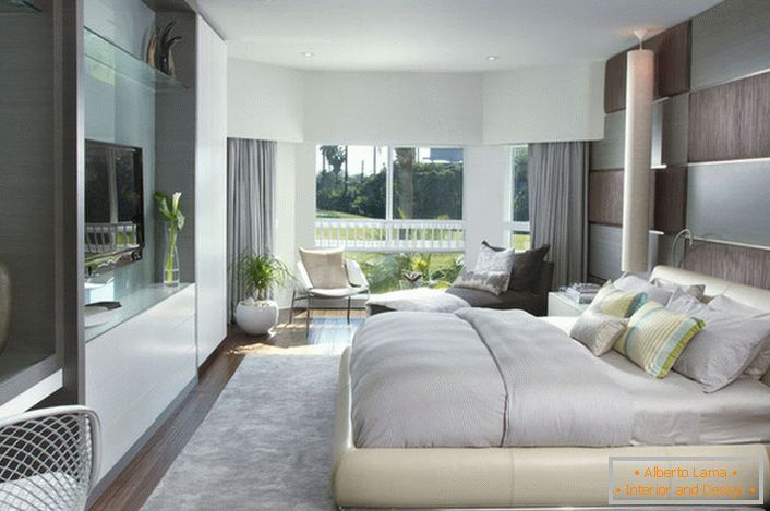 Pat moale, în vrac, în dormitor într-un stil modern. Mobilierul cu o suprafață lucioasă se potrivește bine cu compoziția generală a interiorului.