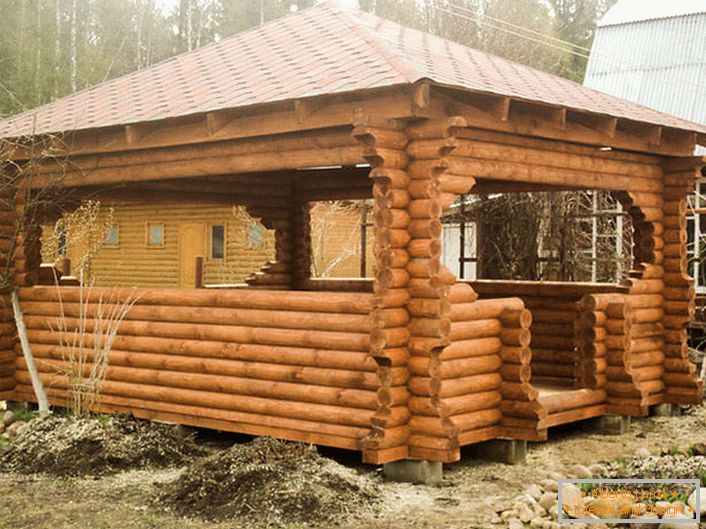 Un cadru din lemn este cel mai potrivit material pentru a face un arbore pentru un teren în stilul unei cabane. Acoperișul din plăci de teracotă arată organic pe fundalul unui copac în vârstă.