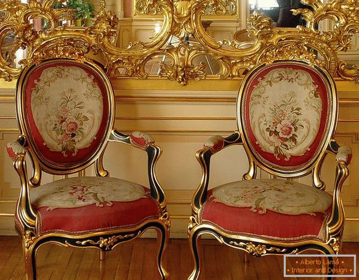 Sculptură stuccoasă de culoare aurie pe oglindă și scaune cu tapițerie roșie moale - reprezentanți strălucitori de stil baroc.